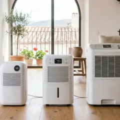 Tres deshumidificadores blancos en un suelo de madera. Uno de ellos muestra "48% Humidity", indicando que un deshumidificador enfria el ambiente.