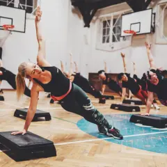 Grupa ćwiczy pilates na stepach, wzmacniając mięśnie głębokie. Ćwiczenia te pomagają w poprawie postawy i elastyczności.