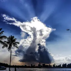 Dramatische Wolkenformationen im Himmel, die an eine engelhafte Gestalt erinnern, über einer Stadtkulisse mit Palmen. Ein Zeichen des Christentums?
