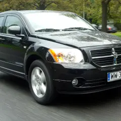 Czarny Dodge Caliber jedzie po mokrej drodze.