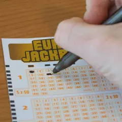 Dłoń zaznacza liczby na kuponie Eurojackpot. Zastanawiasz się, jak skreślić Eurojackpot? To proste!