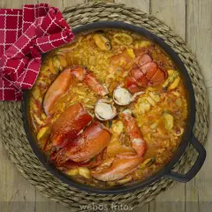Paella de marisco con langosta, mejillones y calamares, servida en una paellera sobre una esterilla de mimbre.