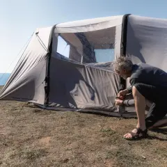 Mężczyzna rozbija namiot na trawiastym klifie nad morzem. Czy można rozbić namiot na plaży? To miejsce wygląda idealnie.