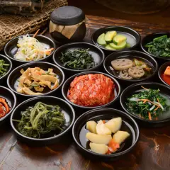 Bogactwo koreańskich **banchan**: kimchi, marynowane warzywa, sałatki z ziół i wiele innych, podane w małych miseczkach.