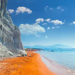Ein atemberaubender Kefalonia Strand mit leuchtend orangefarbenem Sand, der von einer steilen weißen Klippe eingerahmt wird. Das türkisfarbene Meer lädt zum Schwimmen ein.