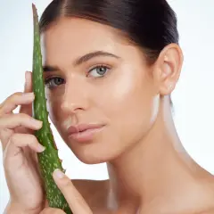 Una mujer joven con piel radiante sostiene una hoja de aloe vera, demostrando que el aloe vera es bueno para la cara.