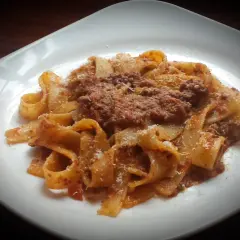 Pappardelle ragu z parmezanem na białym talerzu.