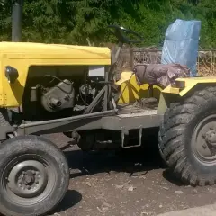 Żółty, stary ciągnik rolniczy, prawdziwy esiok, stoi na uboczu. Jego masywne opony i widoczny silnik świadczą o jego mocy.