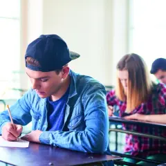 Ragazzo con cappellino scrive concentrato durante un esame. Il suo **did inglese** è importante per il futuro.