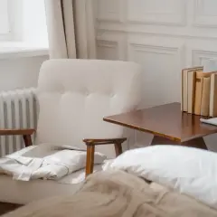 Przytulny pokój z fotelem, łóżkiem i stolikiem nocnym. Grzejnik pod oknem sugeruje, ile wat grzejnika na m2 jest potrzebne do komfortu.