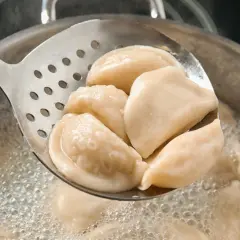 Gorące pierogi z serem, gotowane według przepisu babci, wyjmowane łyżką cedzakową z bulgoczącego garnka.