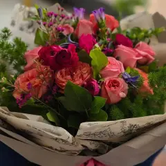 Piękny bukiet różowych i czerwonych róż, ozdobiony zielenią i drobnymi fioletowymi kwiatkami. Idealne kwiaty dla mamy, by sprawić jej radość.