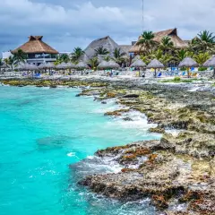 Plage mexicaine avec eau turquoise, rochers, palmiers et bungalows à toit de chaume.