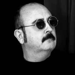 Carlos Areces, con su pareja de gafas redondas y bigote, posa con misterio.