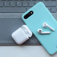 Telefon w turkusowym etui i białe słuchawki bezprzewodowe na klawiaturze. Idealne do tworzenia rankingu słuchawek bezprzewodowych.