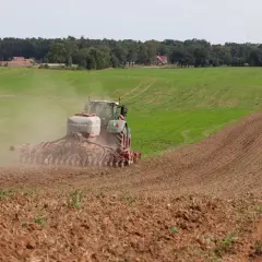 Traktor z siewnikiem HORSCH rozsiewa nawóz, prawdopodobnie fosforan, na polu. W tle las i domy.