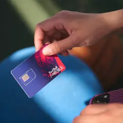 Dłoń trzyma kartę SIM Red Bull MOBILE, gotową do podróży po Europie. Internet na wyciągnięcie ręki!