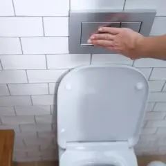 Mano presionando el botón de descarga de los tipos de cisternas wc empotradas.