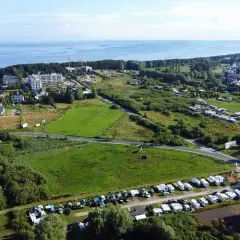Widok z lotu ptaka na pole kempingowe w Kołobrzegu. Widać morze, zabudowania i wiele kamperów oraz przyczep kempingowych.