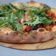 Pyszne, świeżo upieczone ciasto na pizzę z rukolą, oliwkami i papryką, podane na drewnianej desce.