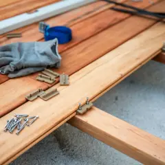 Budowa tarasu drewnianego: wkręty, klipsy montażowe, rękawica i wiertarka na deskach.