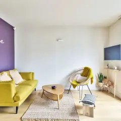 Ein gelbes Sofa und ein Korbsessel mit gelber Decke harmonieren perfekt mit der lila Wand. Welche Farbe passt zu lila? Hier sieht man, dass Gelb eine tolle Wahl ist!