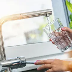 Une main verse de l'eau fraîche du robinet dans un verre. Une idée simple pour comment refroidir de l'eau rapidement.