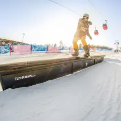 Snowboardzista na grindboxie w **Jaworzynie Krynickiej snowparku**. W tle kolejka linowa i inni narciarze.