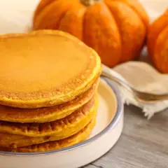 Pila de torrijas de calabaza doradas y esponjosas, con calabazas decorativas al fondo.
