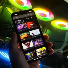 Przeglądanie listy gier na GeForce Now na telefonie, w tle świecące wentylatory komputera.