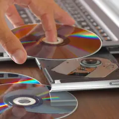 Dłoń wkłada płytę CD do napędu laptopa. Program cdburnerxp pomoże nagrać dane.