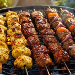 Brochettes de viande grillée, poulet et bœuf, sur un barbecue. Les braises rougeoient sous la grille.