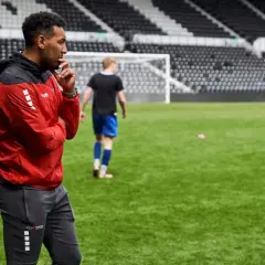 Ein Mann in Rot und Schwarz beobachtet aufmerksam junge Fußballer auf dem Trainingsplatz. Ein typischer Tag im Leben eines Fußball Scout.