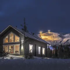 Trillevallen hotell, ett mysigt hus i snölandskap med upplysta skidbackar i bakgrunden.