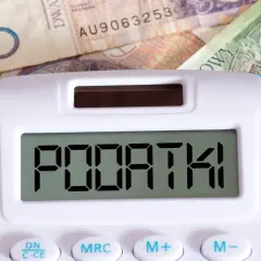 Kalkulator z napisem "PODATKI" na tle polskich banknotów. Czas na rozliczenie PIT 28 druk.