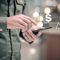Dłoń trzyma telefon, na ekranie symbol dolara i rubla na wadze. Symbolizuje to paypal przewalutowanie.