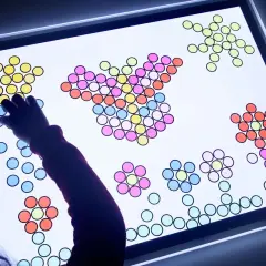 Niño/a creando figuras con piezas de colores sobre una mesa de luz, fomentando sus actividades creativas.