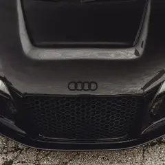 Przód czarnego auta sportowego z maską z włókna węglowego. Widać reflektory, grill i logo Audi.