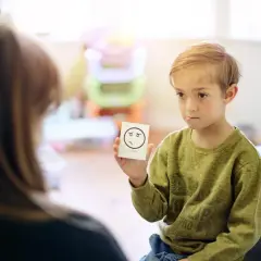 Chłopiec trzyma kartkę z rysunkiem smutnej buźki i napisem "SORRY".