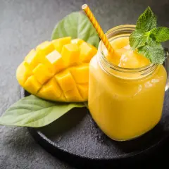 Un smoothie mangue onctueux dans un pot en verre, garni de menthe fraîche, à côté d'une moitié de mangue coupée en dés.