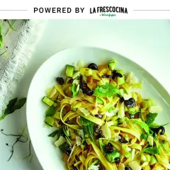 Pasta con verduras frescas, aceitunas negras y queso rallado, servida en un plato blanco.