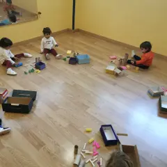 Niños pequeños exploran materiales diversos, cajas y pinzas, aprendiendo sobre el juego heurístico.