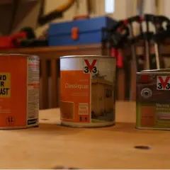 Trois boîtes de produits pour bois : un fondur avant vernis Blanchon, une lasure Classique V33 et un vernis Satin V33.