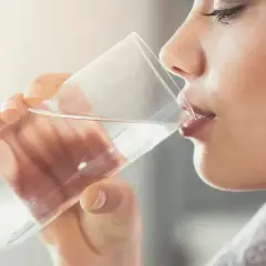 Kobieta pije wodę z kieliszka. Dowiedz się, jak usunąć chlor z wody, aby cieszyć się jej czystym smakiem.