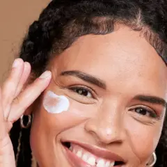 Lächelnde Frau trägt eine Creme auf, die für die vitamin c haut gedacht ist.