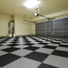 Nowe, czarno-szare płytki w garażu tworzą szachownicę. Widać bramę garażową i bojler.
