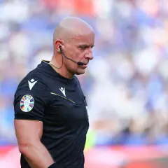 Sędzia Michael Oliver w czarnej koszulce z naszywką Ligi Mistrzów, skupiony na boisku.