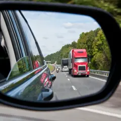 Reflejo en el espejo retrovisor: un camión rojo y una moto circulan por la carretera. ¡Atención! una moto puede adelantar por la derecha.