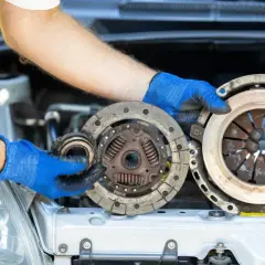 Mechanik w niebieskich rękawiczkach pokazuje zużyte części sprzęgła. Poznaj wymiana sprzęgła koszt i dowiedz się, kiedy warto je wymienić.