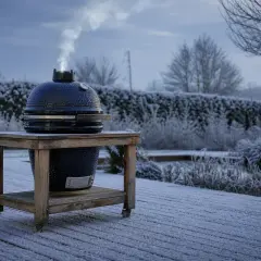 Un barbecue d'hiver fume sur une terrasse enneigée, défiant le froid pour un repas en plein air.
